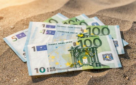 Aufgef&auml;cherte Euro-Geldscheine auf Strandsand im Sonnenuntergang als Symbol f&uuml;r den OnlySpins Fiat-Willkommensbonus