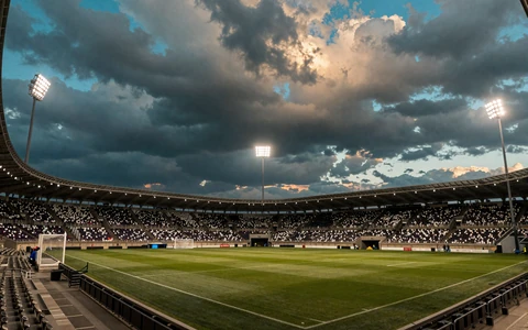 Stadion-Flutlicht bei D&auml;mmerung mit t&uuml;rkis-goldenem Sturmhimmel als Symbol f&uuml;r den OnlySpins Sportsbook